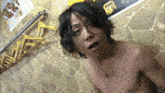 a shirtless man is standing in front of a stone wall with a sign that says ' tokyo ' on it