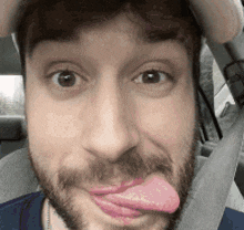 a man with a beard is sticking his tongue out while wearing a seat belt .