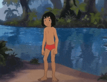 a boy in a red shorts is standing next to a body of water .