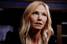 a woman with blonde hair and blue eyes is wearing a black jacket and looking up