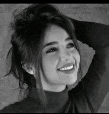 a woman is smiling in a black and white photo while holding her hair in a bun .