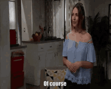 a woman in a blue off the shoulder top is standing in a kitchen and says of course