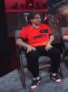 a man sits in a chair with a red shirt that says g2n