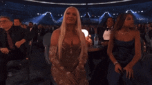 a woman with long blonde hair is sitting in a crowd applauding