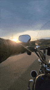 a person riding a motorcycle down a road with the sun setting in the background