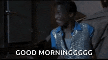 a man in a blue shirt and silver vest is smiling and saying `` good morning gg . ''