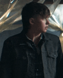 a young man wearing a black jacket and tie is standing in front of a wall with a geometric pattern .