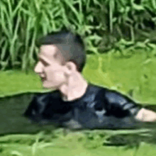 a man is swimming in a pond with a black shirt on .