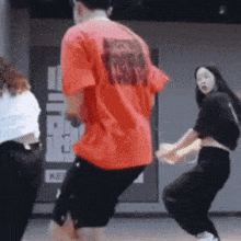 a man in a red shirt is dancing with two women in black pants