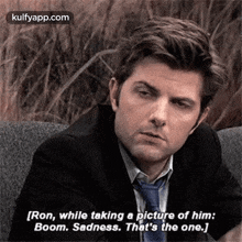 a man in a suit and tie is sitting on a couch talking to another man .