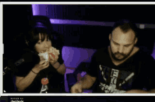 a man and a woman are eating hamburgers in front of a screen that says " denlavic "