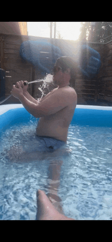 a shirtless man is sitting in a pool drinking from a bottle