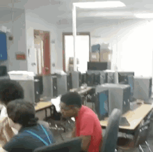 a man in a red shirt is sitting at a desk in a computer lab