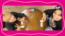 two men are sitting at a table playing a game with the word imp on the bottom right