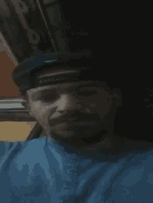 a man with a beard wearing a hat and a blue shirt