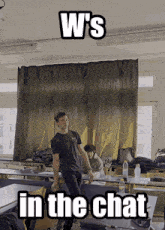 a man in a black shirt stands in front of a curtain with the words w 's in the chat written on it