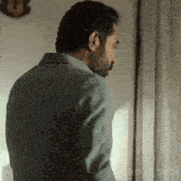 a man with a beard is standing in front of a window and looking out the window .