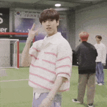 a young man in a pink and white striped shirt is giving a peace sign while standing on a soccer field .