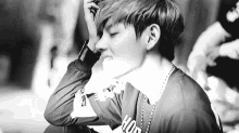 a black and white photo of a young man sitting down with his hands on his head .