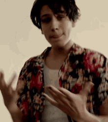 a young man wearing a floral shirt is clapping his hands in a room .