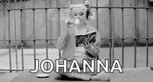 a black and white photo of a woman sitting on the ground reading a book and drinking coffee .