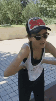 a woman wearing a baseball cap and sunglasses is standing on a sidewalk