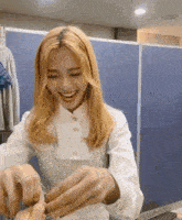 a woman with blonde hair and a white shirt is smiling while holding something in her hands .