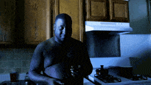 a shirtless man stands in a kitchen with a stove top oven