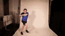 a man in a blue shirt is holding a sword in front of a white wall