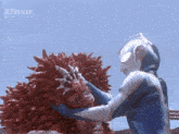 a man in a blue suit is holding a large red monster in his hands .
