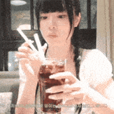 a girl is holding a glass of soda with a straw in her hand .