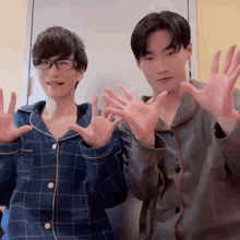 two young men wearing pajamas are standing next to each other and making funny faces with their hands .
