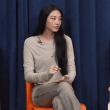 a woman with long black hair is sitting in a chair holding a cell phone