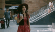 a woman in a red dress stands in front of an escalator and a sign that says ' gifselarroni ' on it