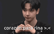 a young man is making a heart shape with his hands in front of a black background .