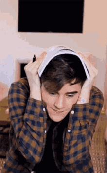 a young man in a plaid shirt is holding a book on his head .