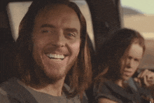 a man with long hair is smiling in a car and the word slim is on the bottom right