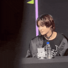 a man sitting at a table with a bottle of water and a sign that says ' i love you '