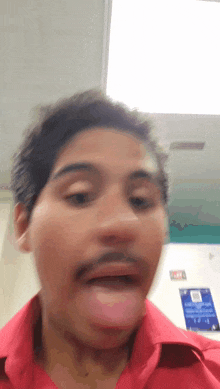 a man with a mustache and a red shirt is sticking his tongue out