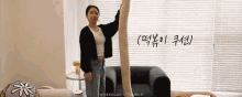 a woman in a black cardigan is standing next to a chair holding a very long piece of fabric .