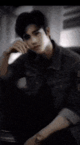 a young man in a denim jacket is sitting down with his hand on his face .