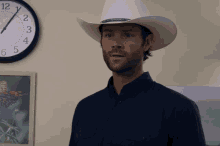 a man wearing a cowboy hat stands in front of a clock that shows the time as 4:20