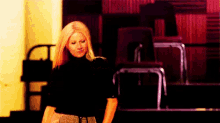 a woman in a black turtleneck is standing in front of a row of chairs .