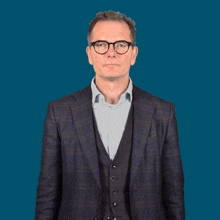 a man wearing glasses and a suit is pointing to his chest