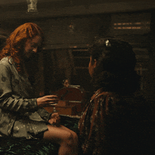 a woman with red hair is sitting next to another woman who is holding a glass