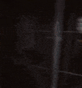 a blurry picture of a man in a blue shirt standing in front of a fence at night .