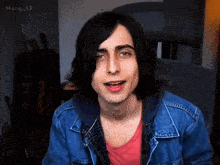 a young man with long hair is wearing a denim jacket and a pink shirt .