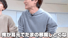 a man in a gray hoodie is talking to another man in a brown sweater