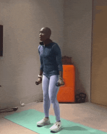 a man is squatting on a yoga mat with dumbbells in his hands
