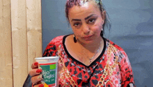 a woman in a red and black leopard print shirt is holding a cup of bio tefföl .